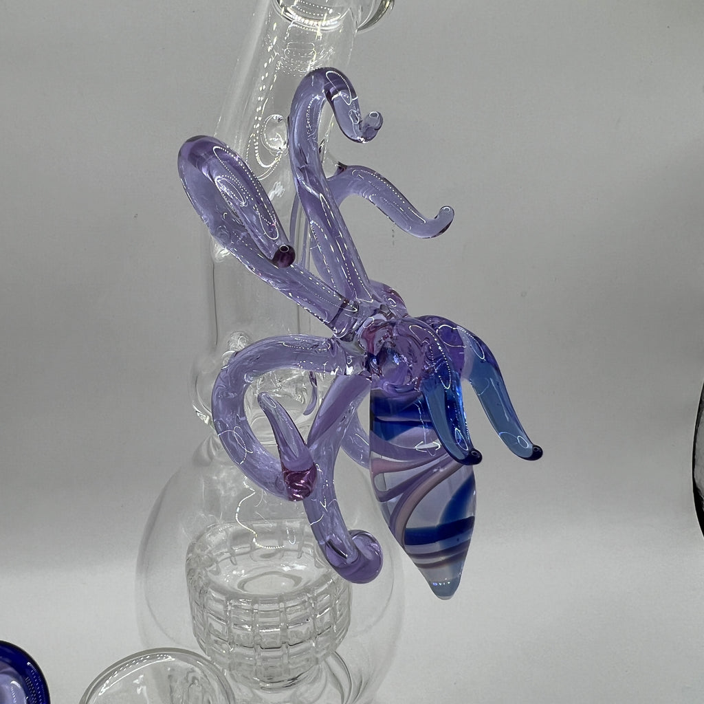 Close up view of handcrafted OTG Glass squid sculpture with flowing tentacles and striped blue body